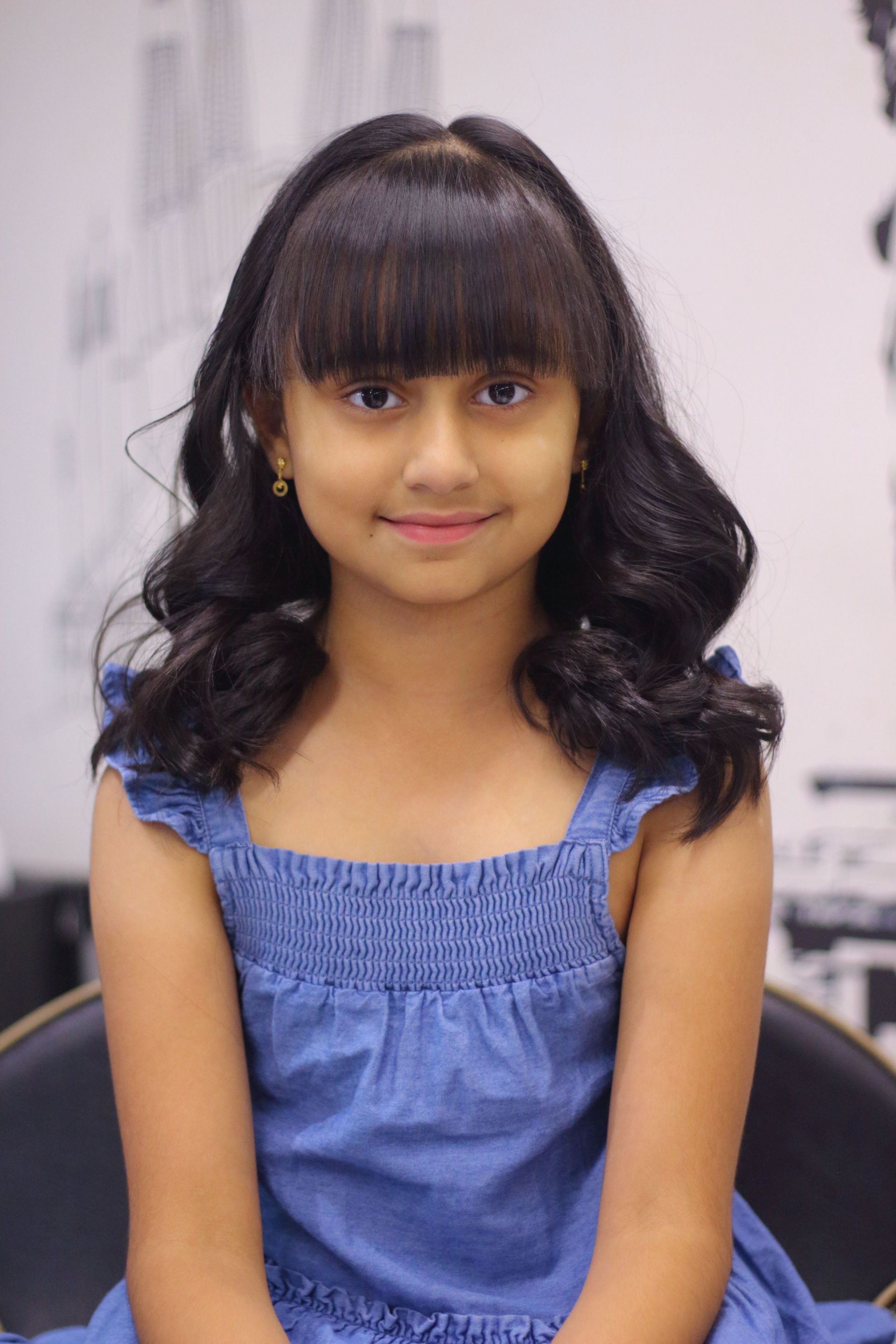 Portrait of a young girl with black hair sitting indoors in a blue dress.